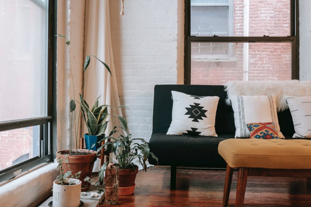 A cozy loft sitting area with a cushioned sofa, a mustard bench, and potted plants by sunlit windows