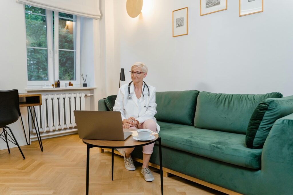 A clinician in a white coat with a stethoscope working on a laptop for a telehealth visit