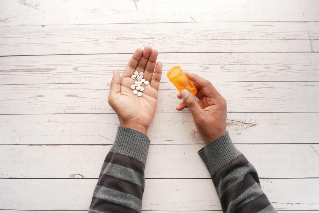Hands holding white tablets in one palm and an orange prescription bottle in the other